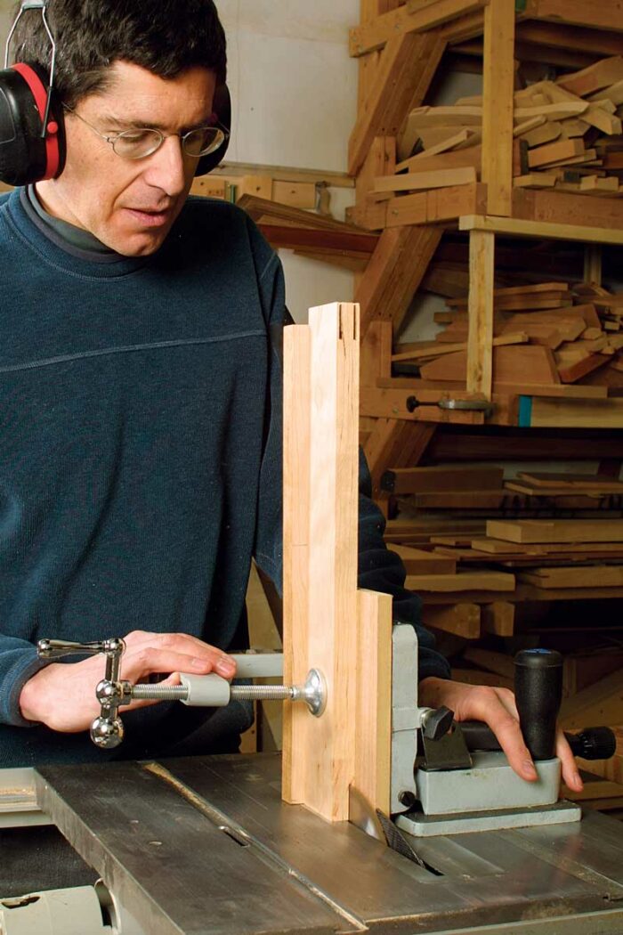 Clamp the spacer in the jig and against the scrap stock in back. Adjust the jig to line up with the tenon mark, then cut the first cheek.