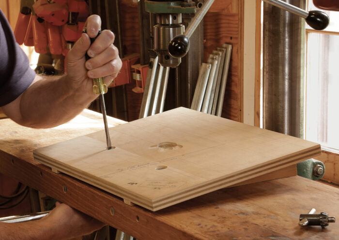 Add a ramp and tilt the table to drill at the correct rake and splay angles. To tilt the seat blank to the rake angle, Durfee screws a plywood ramp to his drill-press table. 