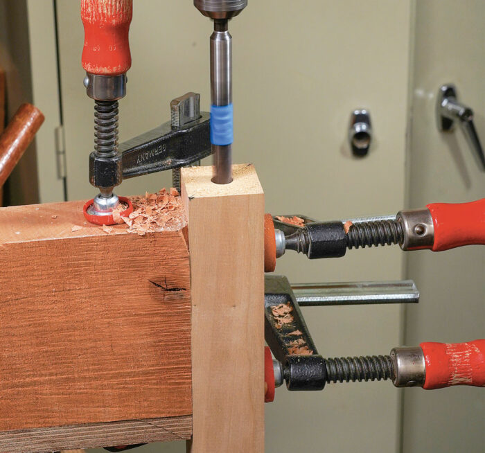 Drill for dowels. Move the drill-press table to one side and clamp on a square block as shown to hold the parts vertically. Drill at least 1-1⁄2 in. into each part.